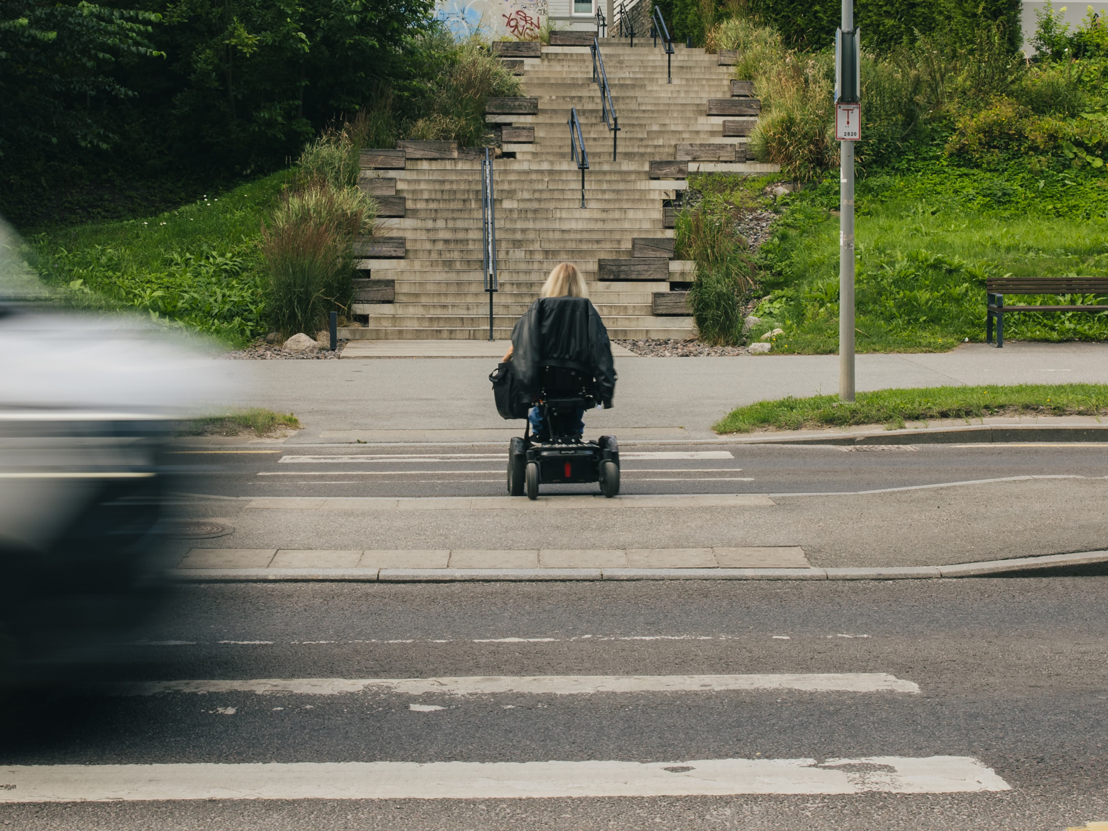 Powerchair user at a crosswalk facing a staircase without a ramp